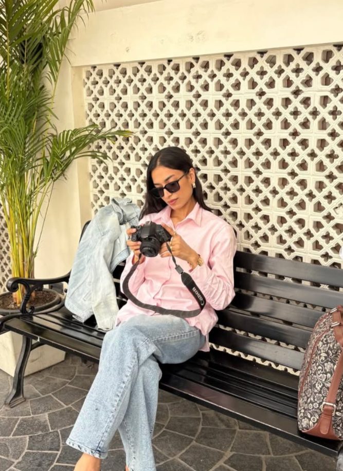 Garima wearing the Morning Pink shirt, sitting on a bench with a camera