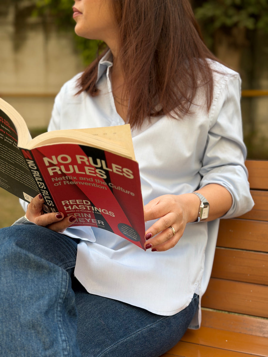 Person reading a book titled 'No Rules Ruin' by John U. Nef on a wooden bench.