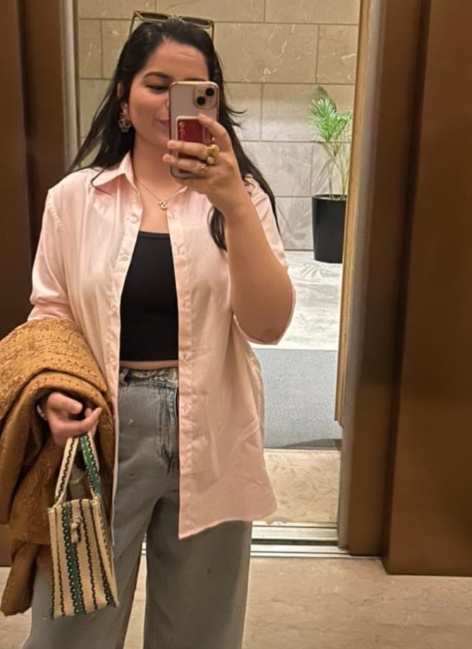 Shuvenih wearing the Morning Pink shirt open over a black top